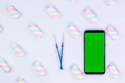 Phone mockup. Syringe with needle and black smartphone with blank screen. White background with twisted marshmallow pattern.