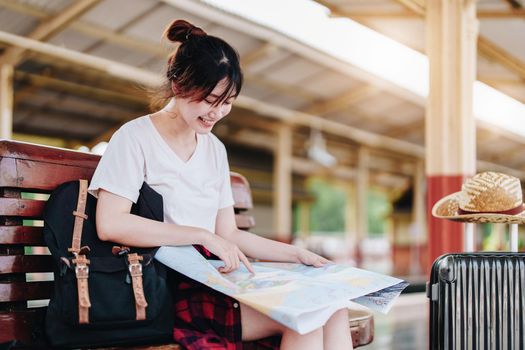 summer, relax, vacation, travel, portrait of a cute Asian girl looking at a map to plan a trip while waiting at the train station