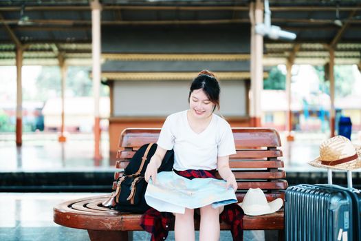 summer, relax, vacation, travel, portrait of a cute Asian girl looking at a map to plan a trip while waiting at the train station