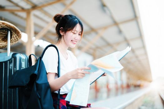 summer, relax, vacation, travel, portrait of a cute Asian girl looking at a map to plan a trip while waiting at the train station