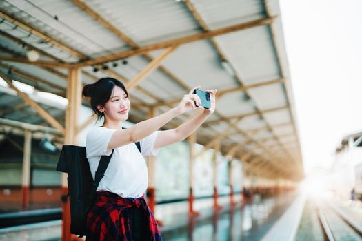 summer, relax, vacation, travel, portrait of beautiful Asian girl using the smartphone mobile take a photo selfie face yourself at the train station while waiting for their travel time