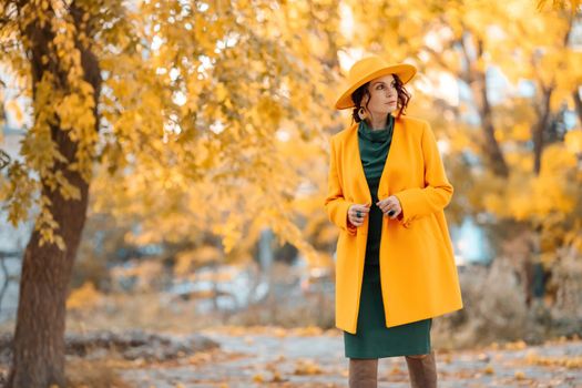 Beautiful woman walks outdoors in autumn. She is wearing a yellow coat, yellow hat and green dress. Young woman enjoying the autumn weather. Autumn content.