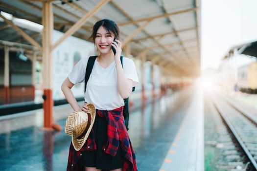 summer, relax, vacation, travel, portrait of beautiful Asian girl using the smartphone mobile to call friends at the train station while waiting for their travel time