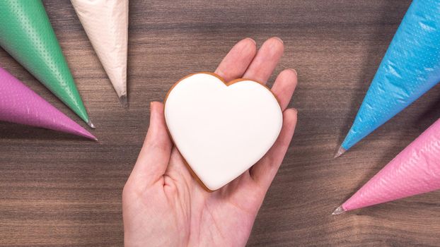 Hand holding white heart shape cookie for Mothers day, Womans day or Valentines Day on wooden background. Copy space.