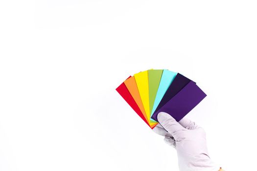 Hand holds a rainbow color palette of paints on a white background. Top view, flat lay. Banner.