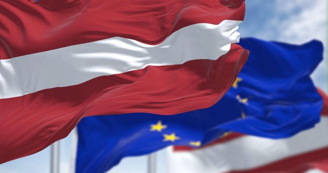 Detail of the national flag of Latvia waving in the wind with blurred european union flag in the background on a clear day. Democracy and politics. European country. Selective focus.