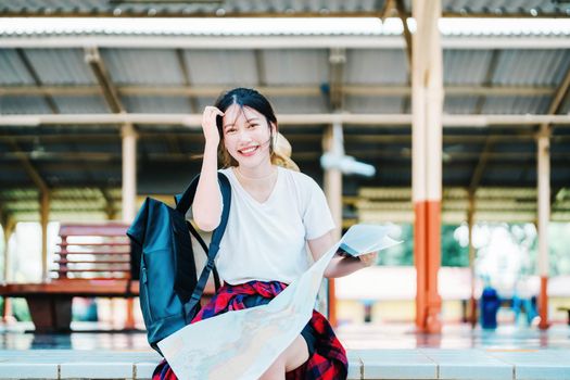 summer, relax, vacation, travel, portrait of a cute Asian girl looking at a map to plan a trip while waiting at the train station