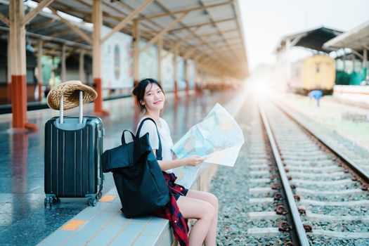 summer, relax, vacation, travel, portrait of a cute Asian girl looking at a map to plan a trip while waiting at the train station