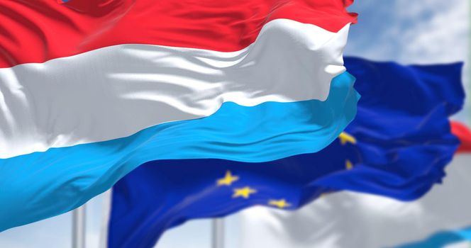 Detail of the national flag of Luxembourg waving in the wind with blurred european union flag in the background on a clear day. Democracy and politics. European country. Selective focus.