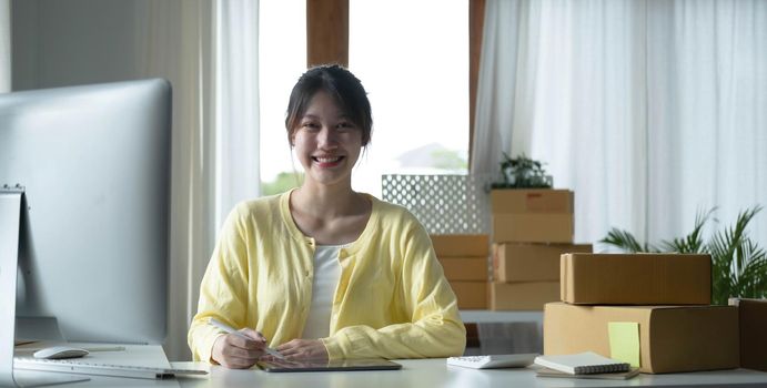 Portrait business Asian woman smile and use tablet checking information on parcel shipping box before send to customer. Entrepreneur small business working at home. SME business online marketing..