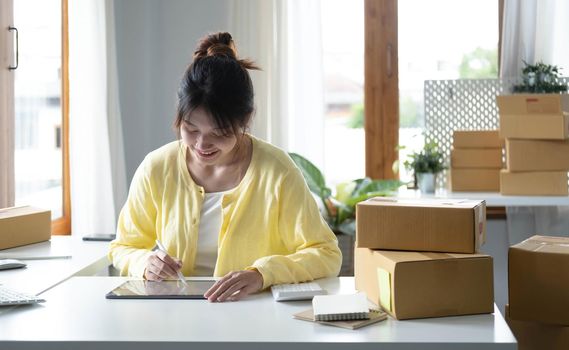 Portrait business Asian woman smile and use tablet checking information on parcel shipping box before send to customer. Entrepreneur small business working at home. SME business online marketing..