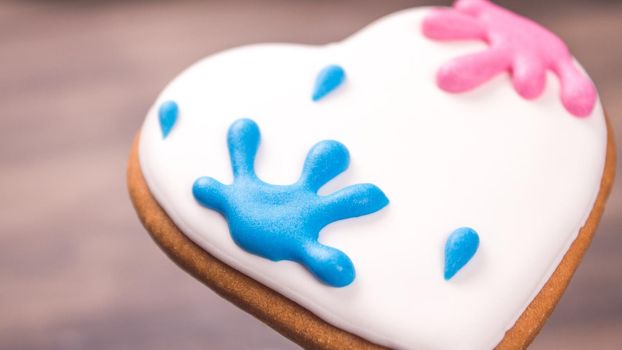 Close view of colorful heart shaped glazed cookie for Valentine's day on wooden background. Paint splatter. Space for text. Macro Easter cookie.