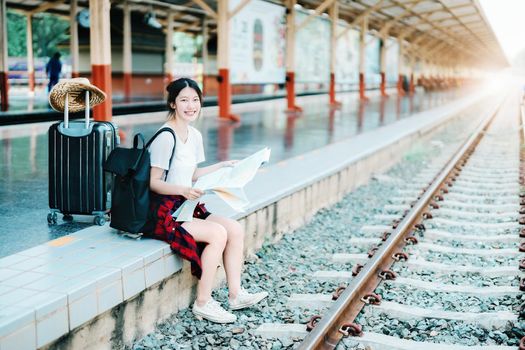 summer, relax, vacation, travel, portrait of a cute Asian girl looking at a map to plan a trip while waiting at the train station