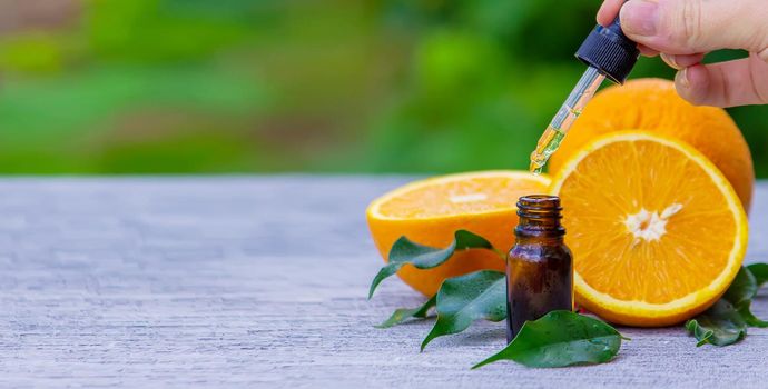 Essential orange oil in a bottle, fresh fruit pieces on the background. Natural flavors. Selective focus