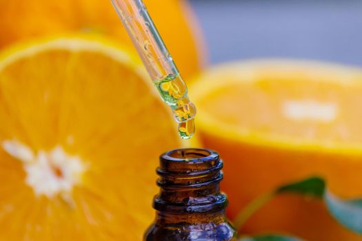 Essential orange oil in a bottle, fresh fruit pieces on the background. Natural flavors. Selective focus