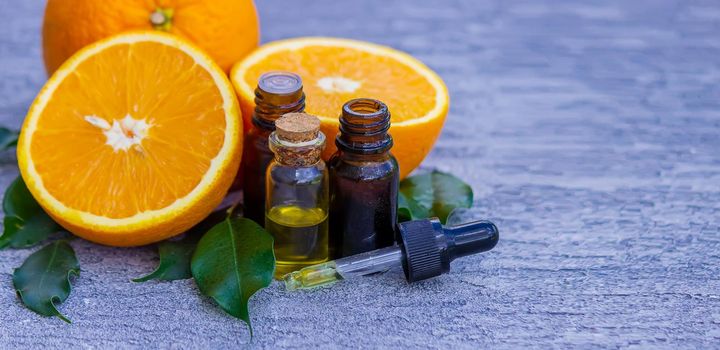 Essential orange oil in a bottle, fresh fruit pieces on the background. Natural flavors. Selective focus