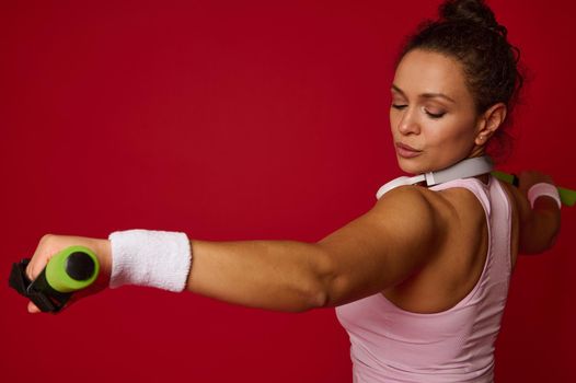 Close-up of young beautiful Hispanic fit sportswoman working out with dumbbells against red colored background with copy ad space. Sport, fitness, healthy and active lifestyle, weight loss concept