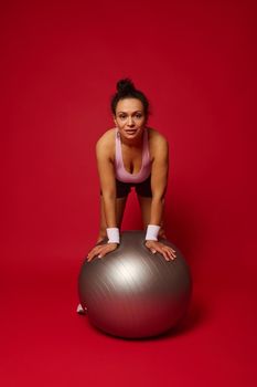 Portrait of a beautiful African American athlete woman with a fit ball isolated over red background with copy ad space
