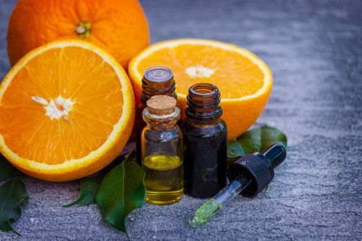 Essential orange oil in a bottle, fresh fruit pieces on the background. Natural flavors. Selective focus