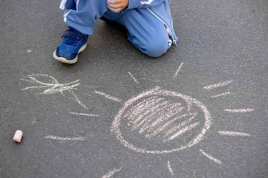 Cute little child draws the sun with chalk outdoors, summer time, chalk. Selective focus. Nature