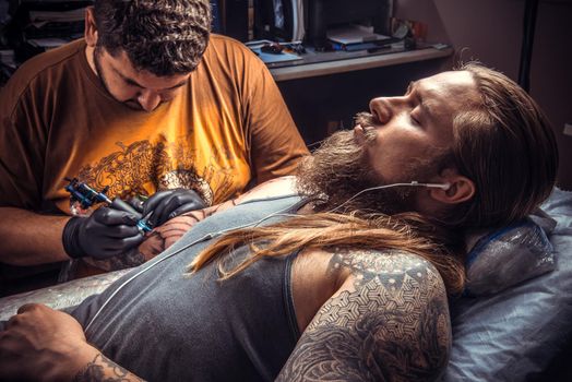 Tattoo artist doing tattoo in salon. Master makes tattoo pictures in tatoo salon.
