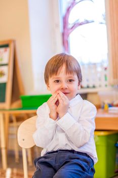 Elegantly dressed in a white shirt, a little boy is sitting in the classroom for lessons. portrait of a boy, blonde hair