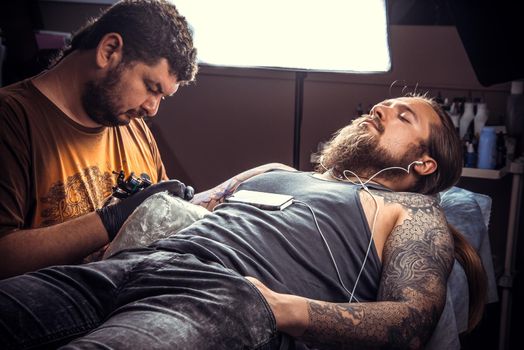 Man wearing gloves makes tattoo pictures in studio./Tattoo specialist create tattoo in tattoo studio.
