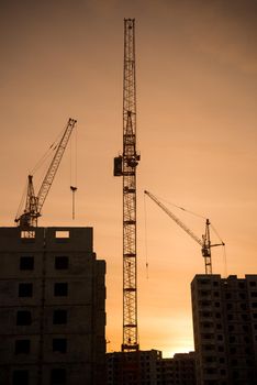 Background of silhouette building crane lift loads with sun set rays yellow cloudy evening sky backdrop Construction site at orange sunset.