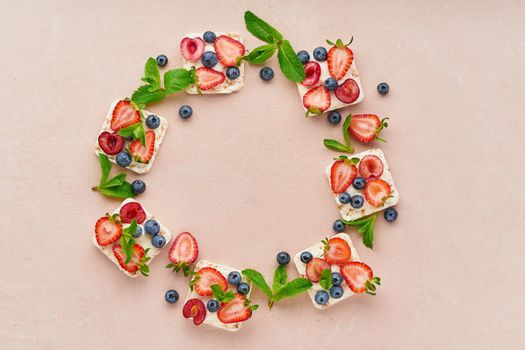 vegeterian dieting rise crispbread frame with berries: strawberry, blueberry, bilberry, blackberry and banana on pastel terracotta background top view