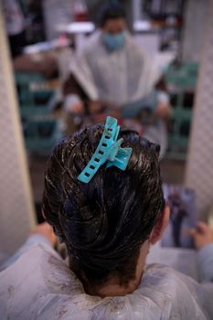 young woman with hair clip on her head, waiting in front of the mirror while the hair dye dries