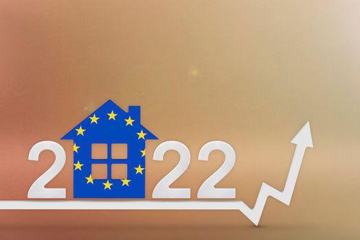 The cost of real estate in Europe in 2022. Rising cost of construction, insurance, rent in Europe. House model painted in flag colors, up arrow on yellow background.