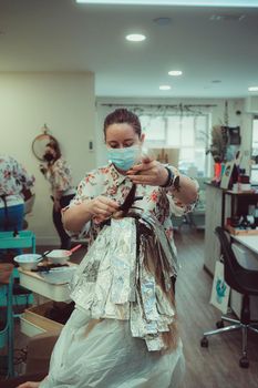 Blonde woman dying her hair in beauty salon. Close-up of her hair coloring. Use of aluminum foil to highlight.