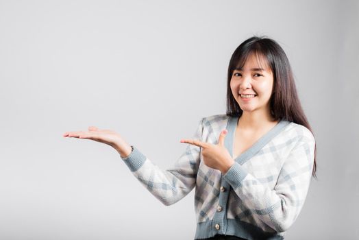 Smiling happy woman presenting product holding something on palm away side, Portrait Asian beautiful young female show hand demonstrate gesture studio shot isolated on white background with copy space