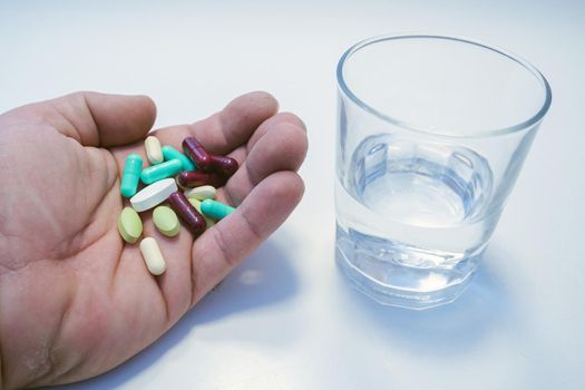 man's hand with pills in front of glass of water