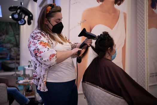 Hair stylist drying client's hair with comb and hair dryer in beauty salon