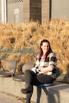 Young woman posing sitting on a bench, wearing a plaid shirt and reddish hair. casual look