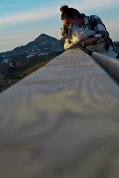 young woman posing with her dog on a wooden railing with mountains in the background. blur background