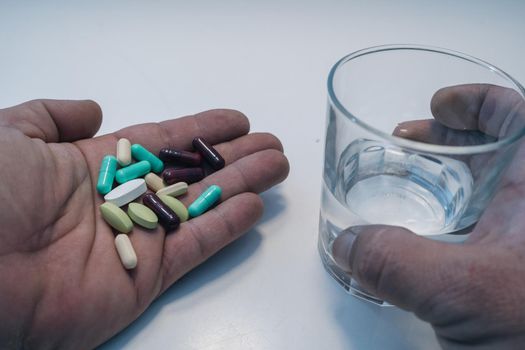 man's hand with pills in front of glass of water