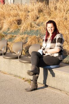 Young woman posing sitting on a bench, wearing a plaid shirt and reddish hair. casual look