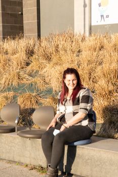 Young woman posing sitting on a bench, wearing a plaid shirt and reddish hair. casual look
