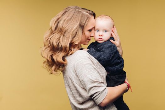 Full length studio portrait of gorgeous elegant brunette mom in denim dress with lovely laughing son on her hands. They smiling at camera.