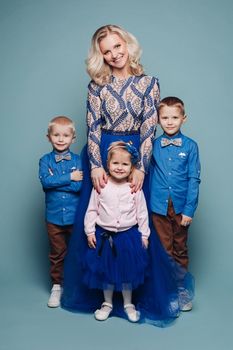 Studio portrait of happy smiling family of five posing and looking at camera together. Cheerful father embracing his children. Isolate on blue.