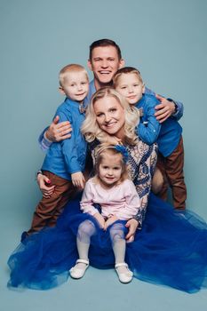 Studio portrait of happy smiling family of five posing and looking at camera together. Cheerful father embracing his children. Isolate on blue.