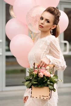 Headshot of gorgeous brunette woman with flawless skin, high hairdo, professional make up and bunch of pink flowers looking at camera. Unfocused pink background.