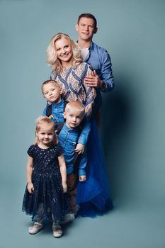 Studio portrait of happy smiling family of five posing and looking at camera together. Cheerful father embracing his children. Isolate on blue.