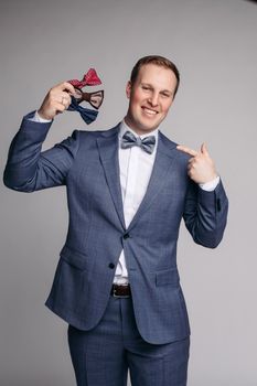 Selective focus of smiling man keeping bow ties in hand on isolated background. Young man wearing smart suit and white shirt looking at camera and posing in studio. Concept of official clothes.