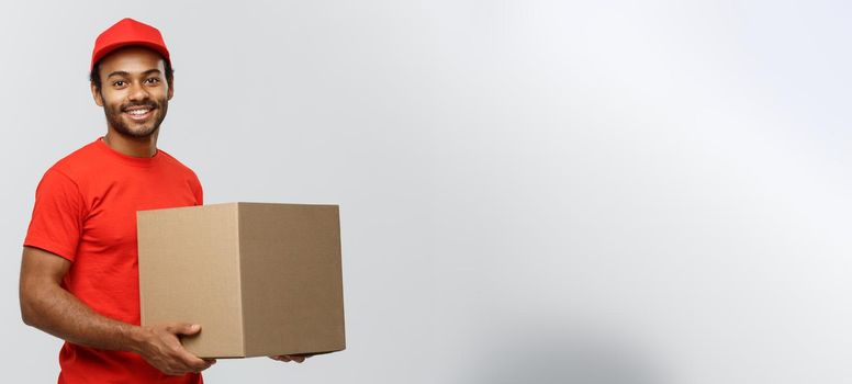 Delivery Concept - Portrait of Happy African American delivery man in red cloth holding a box package. Isolated on Grey studio Background. Copy Space