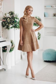 Gorgeous pretty lady stay in luxury apartment. Beautiful young woman in elegant beige dress posing. Happy blonde model relaxing after long working day.