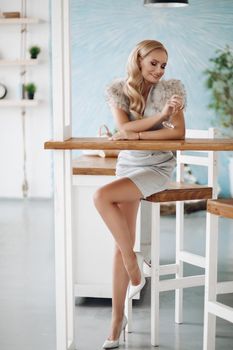 Smiling fashion beautiful woman sitting on bar counter full shot. Happy fashionable young girl at restaurant having positive emotion