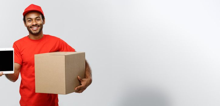 Delivery Concept - Portrait of Handsome African American delivery man or courier with box showing tablet on you to check the order. Isolated on Grey studio Background. Copy Space